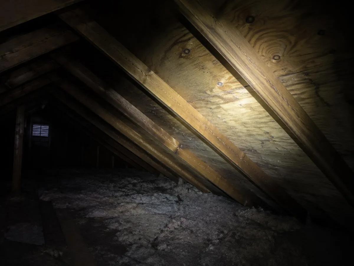 Flashlight beam across attic decking and rafters