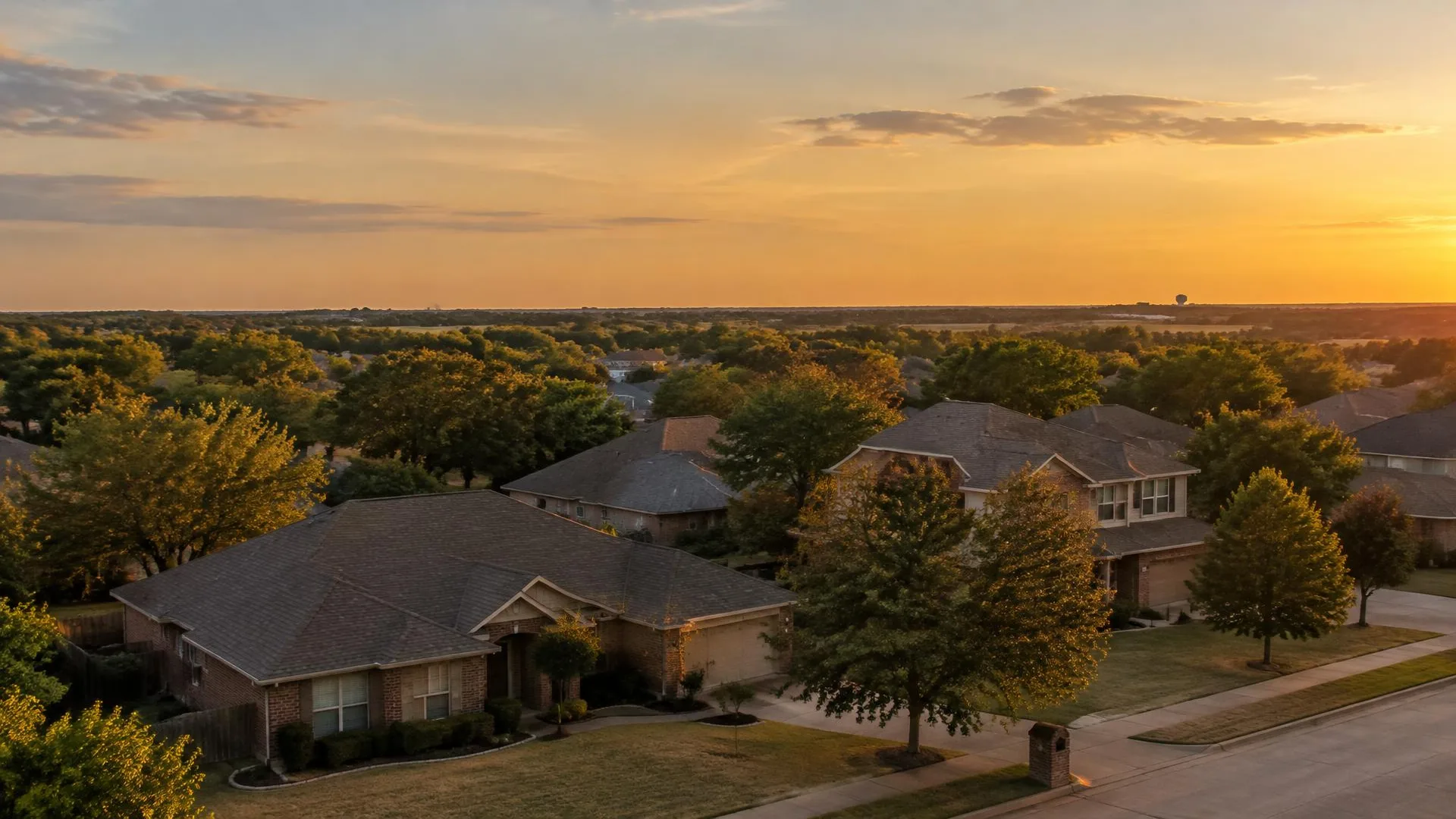 Golden-hour light over suburban rooftops and oak trees