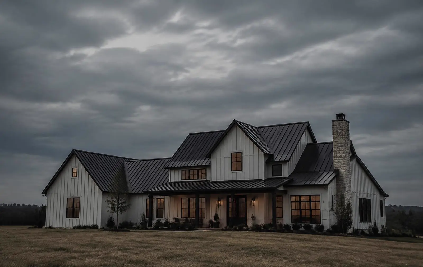White farmhouse with a dark standing-seam metal roof under an overcast sky